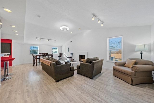 living room featuring track lighting, light hardwood / wood-style flooring, and vaulted ceiling