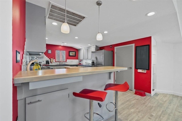 kitchen featuring pendant lighting, a kitchen breakfast bar, light hardwood / wood-style floors, stainless steel fridge, and kitchen peninsula