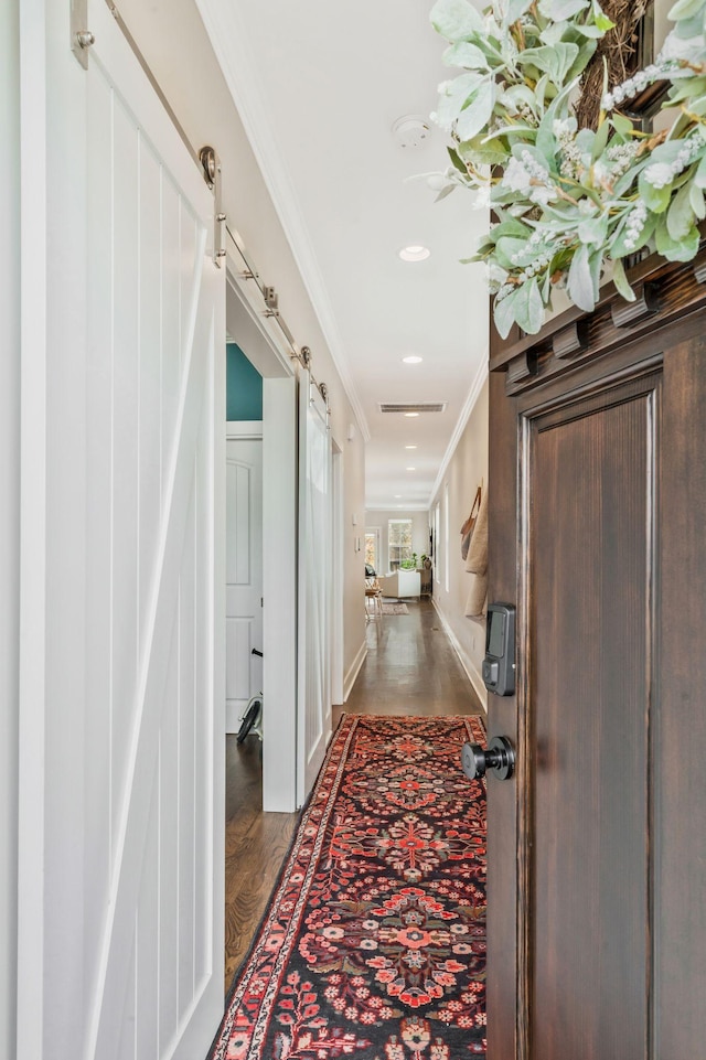 corridor featuring ornamental molding, a barn door, and dark wood-type flooring