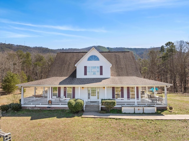 view of front facade featuring a shingled roof, a front lawn, a porch, and a wooded view