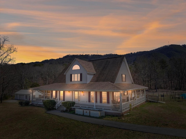 back of house with a wooded view, a porch, a lawn, and fence