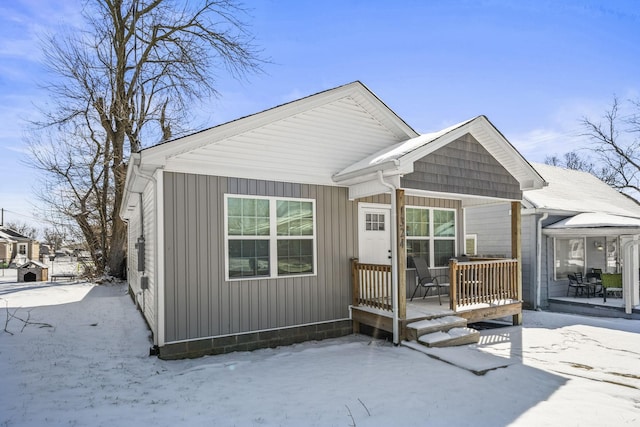 snow covered rear of property with board and batten siding and covered porch