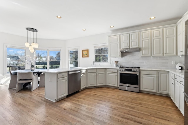 kitchen with appliances with stainless steel finishes, decorative light fixtures, light hardwood / wood-style floors, kitchen peninsula, and white cabinets