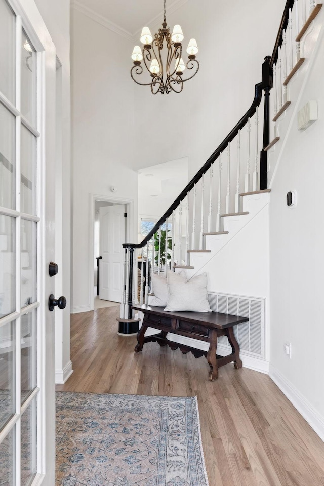 foyer featuring hardwood / wood-style flooring, ornamental molding, a chandelier, and a high ceiling