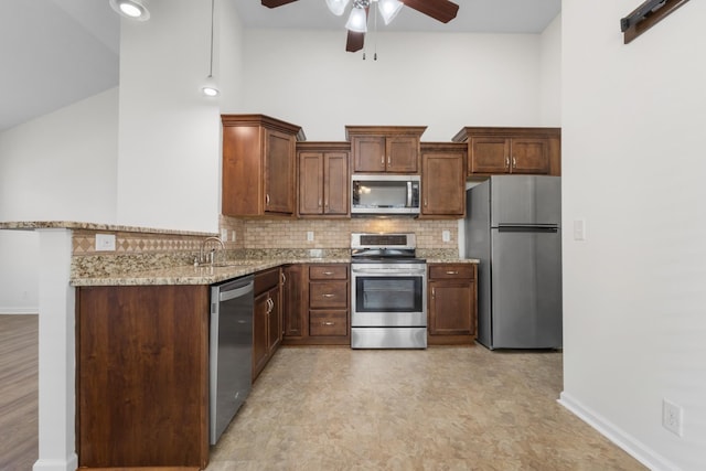 kitchen featuring kitchen peninsula, a towering ceiling, light stone countertops, tasteful backsplash, and appliances with stainless steel finishes