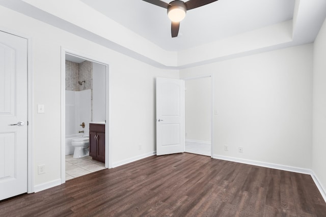 unfurnished bedroom with hardwood / wood-style floors, ceiling fan, ensuite bathroom, and a tray ceiling