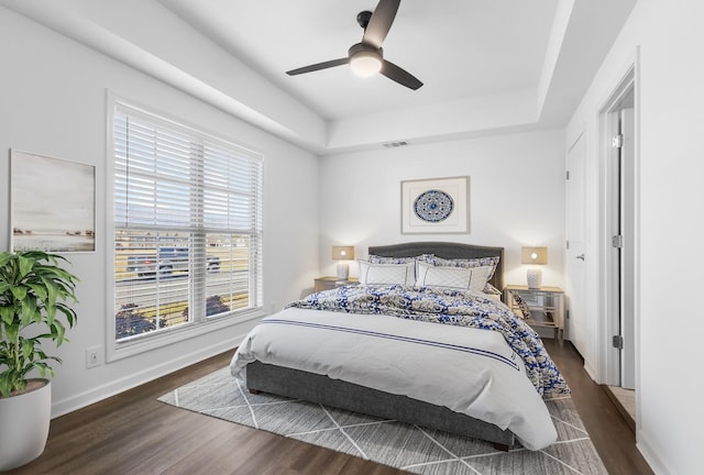 bedroom featuring dark hardwood / wood-style flooring, ceiling fan, and a raised ceiling