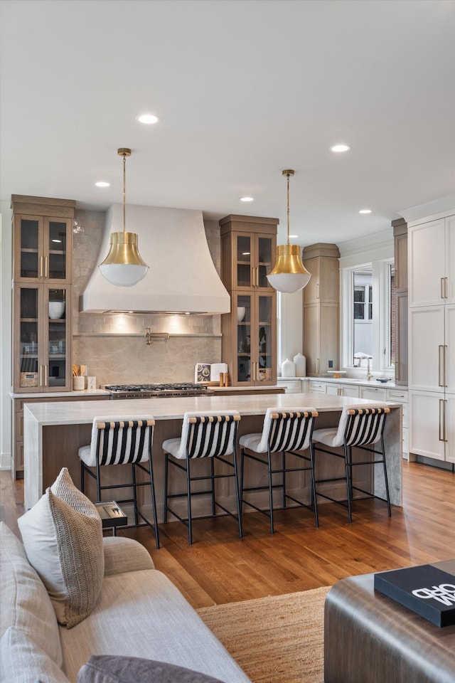 kitchen with hanging light fixtures, a kitchen bar, wood-type flooring, and custom range hood