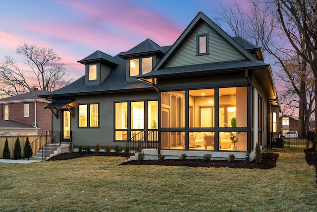 back house at dusk with central AC unit and a lawn