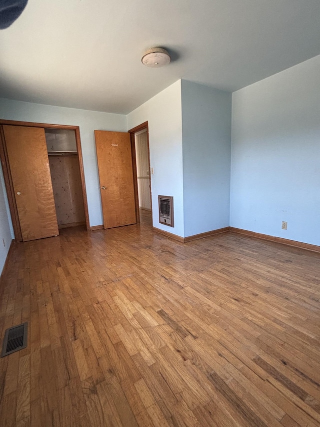 unfurnished bedroom with a fireplace, heating unit, wood-type flooring, visible vents, and baseboards