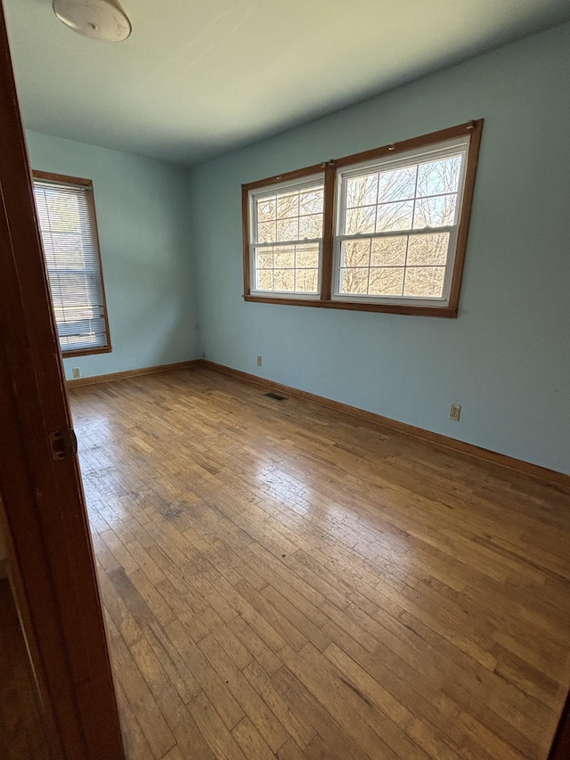 unfurnished room with baseboards, plenty of natural light, visible vents, and hardwood / wood-style floors