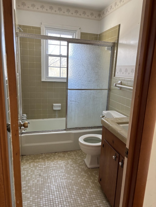 full bathroom with shower / bath combination with glass door, tile walls, toilet, vanity, and tile patterned flooring