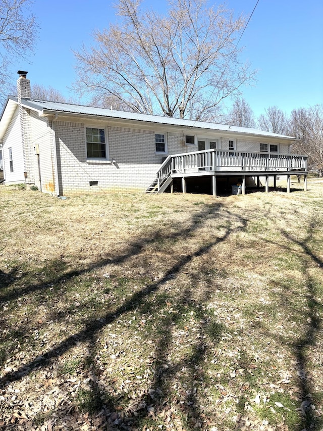 rear view of house featuring a chimney, a deck, a lawn, and brick siding