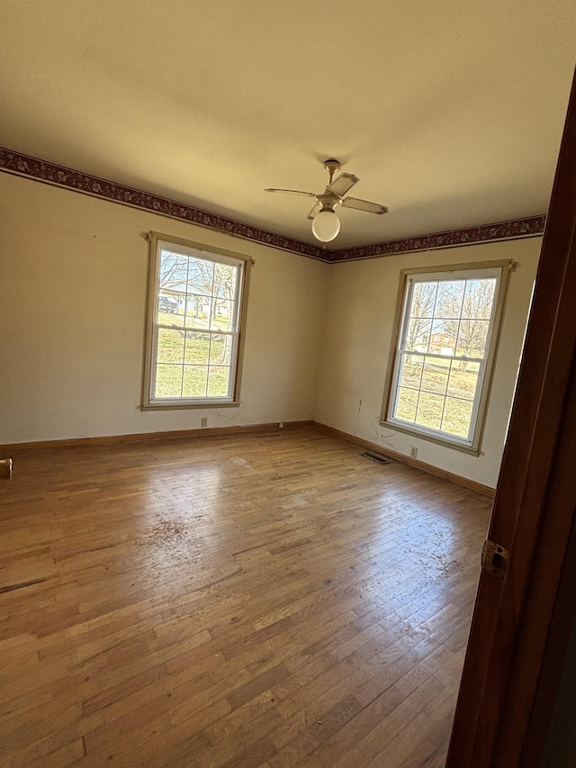 unfurnished room featuring a ceiling fan, visible vents, baseboards, and hardwood / wood-style flooring