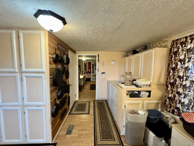 kitchen with a textured ceiling, washing machine and dryer, white cabinetry, and light hardwood / wood-style flooring