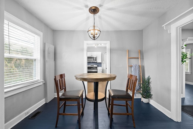 dining space with a textured ceiling, dark wood-type flooring, and a notable chandelier