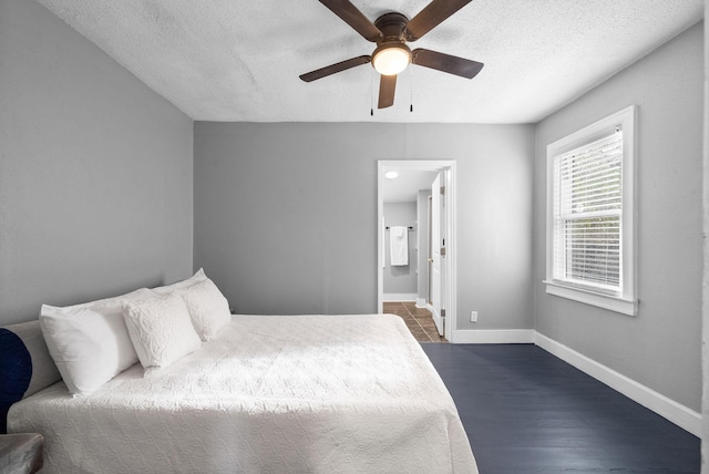 bedroom with ceiling fan, a textured ceiling, connected bathroom, and dark hardwood / wood-style floors