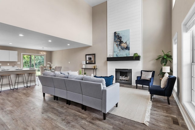 living room with a large fireplace, a towering ceiling, dark hardwood / wood-style floors, and a notable chandelier