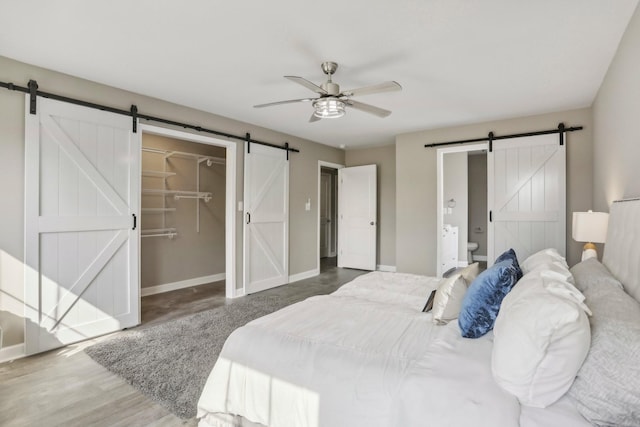 bedroom featuring connected bathroom, dark hardwood / wood-style flooring, a walk in closet, a barn door, and ceiling fan