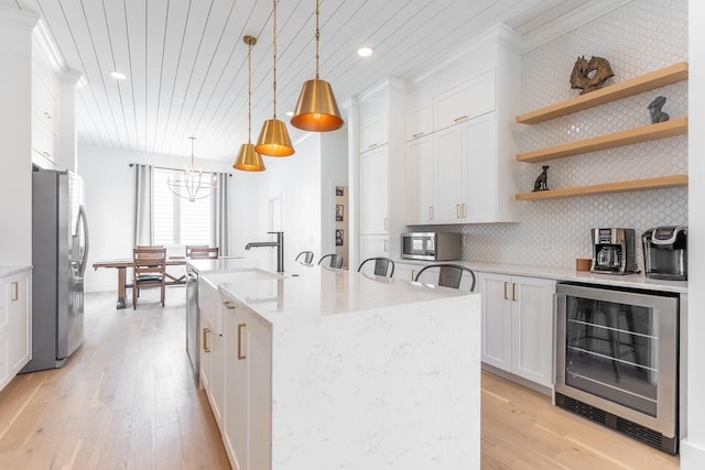 kitchen featuring a center island with sink, hanging light fixtures, stainless steel appliances, white cabinetry, and wine cooler