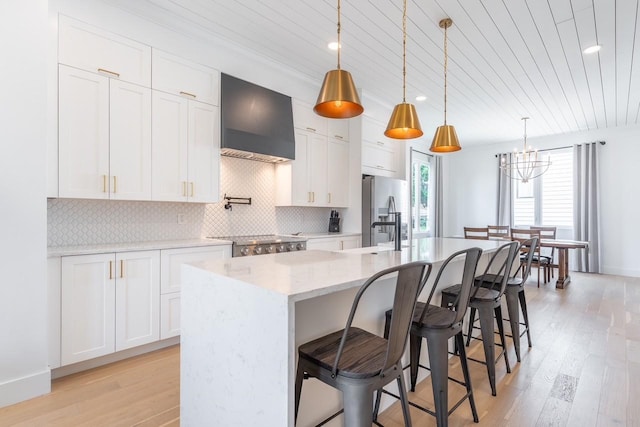 kitchen featuring white cabinetry, a center island with sink, wall chimney exhaust hood, and decorative light fixtures