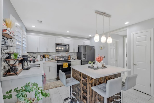 kitchen featuring appliances with stainless steel finishes, tasteful backsplash, a kitchen breakfast bar, white cabinets, and decorative light fixtures