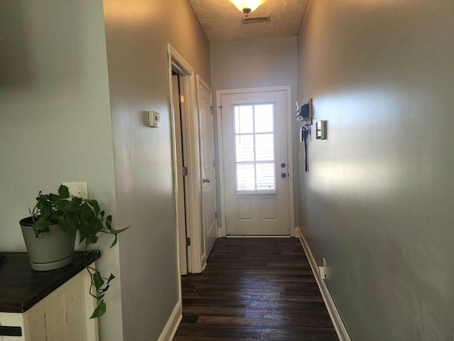 doorway featuring a textured ceiling, dark wood-style floors, visible vents, and baseboards