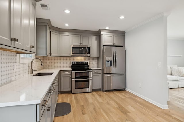 kitchen featuring appliances with stainless steel finishes, sink, gray cabinetry, light hardwood / wood-style floors, and light stone countertops