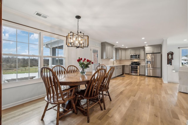 dining area featuring an inviting chandelier, light hardwood / wood-style flooring, crown molding, and sink