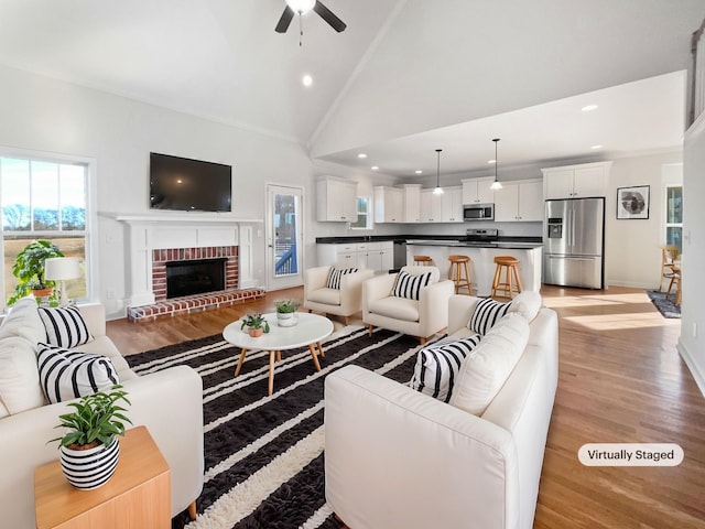 living room with light wood-type flooring, high vaulted ceiling, crown molding, and a fireplace