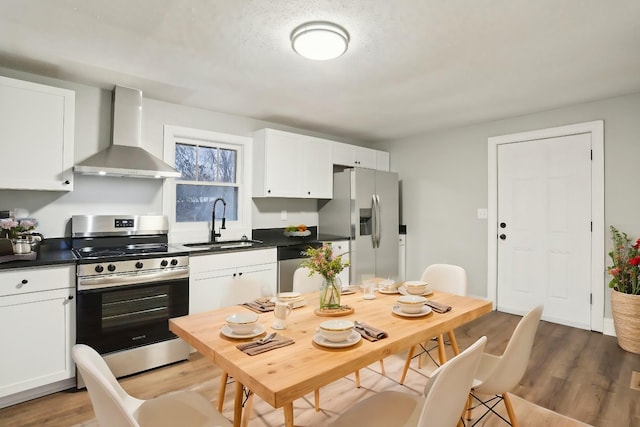 kitchen with sink, white cabinetry, light hardwood / wood-style floors, stainless steel appliances, and wall chimney exhaust hood