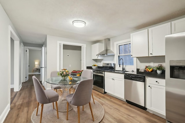 kitchen with dark countertops, wall chimney exhaust hood, stainless steel appliances, white cabinetry, and a sink