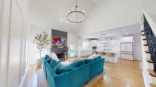 living room featuring high vaulted ceiling, light wood-type flooring, a chandelier, and sink