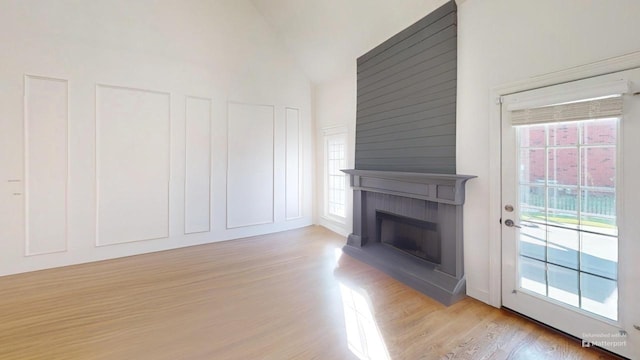 unfurnished living room with light hardwood / wood-style floors, high vaulted ceiling, and a large fireplace