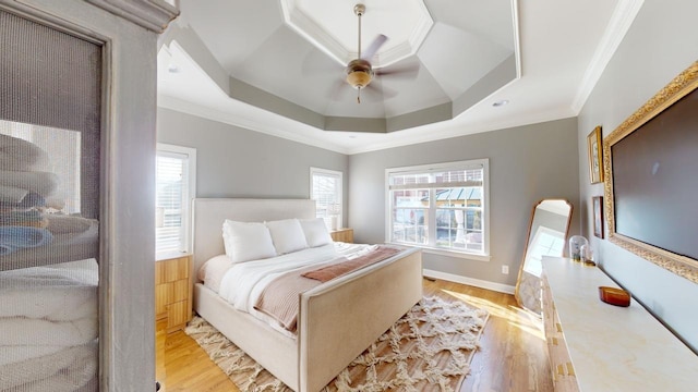 bedroom featuring ornamental molding, light wood-type flooring, a raised ceiling, and multiple windows