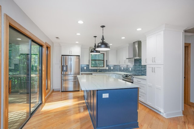 kitchen featuring appliances with stainless steel finishes, white cabinetry, pendant lighting, a kitchen island, and wall chimney exhaust hood