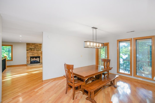 dining space featuring an inviting chandelier, a stone fireplace, and light hardwood / wood-style flooring