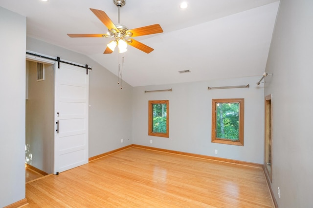 unfurnished room featuring light wood-type flooring, lofted ceiling, ceiling fan, and a barn door