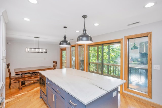 kitchen with stainless steel microwave, a center island, blue cabinets, light wood-type flooring, and hanging light fixtures