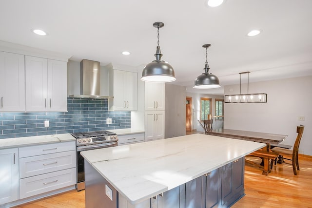 kitchen with wall chimney range hood, decorative light fixtures, gas range, a center island, and white cabinetry