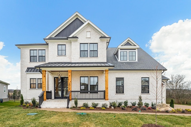 modern farmhouse style home featuring a standing seam roof, covered porch, a front yard, and brick siding