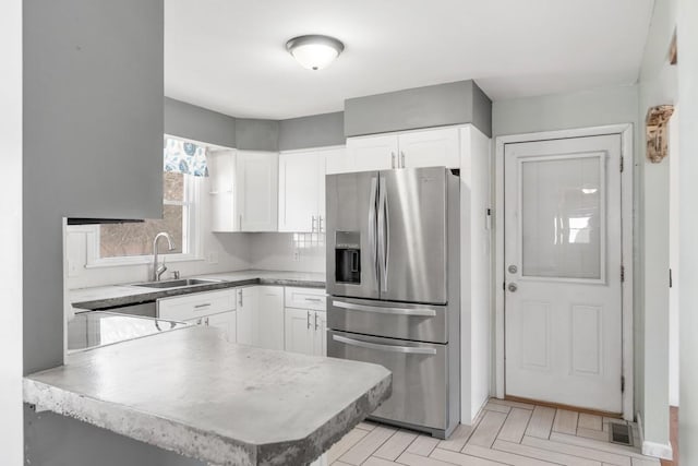 kitchen with white cabinetry, kitchen peninsula, stainless steel refrigerator with ice dispenser, sink, and light parquet flooring