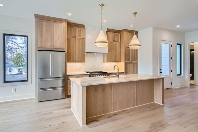 kitchen with a center island with sink, light stone countertops, stainless steel fridge, sink, and backsplash