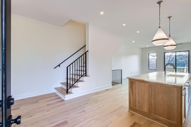 kitchen with a center island with sink, light hardwood / wood-style flooring, sink, pendant lighting, and light stone countertops