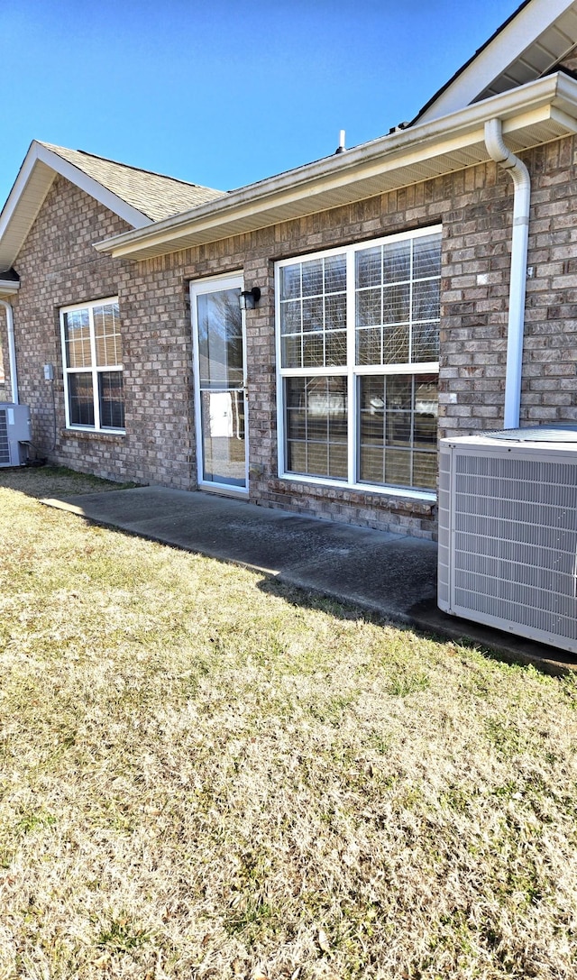 rear view of property with brick siding, cooling unit, and a yard