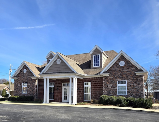 view of front of house featuring stone siding, brick siding, and a shingled roof