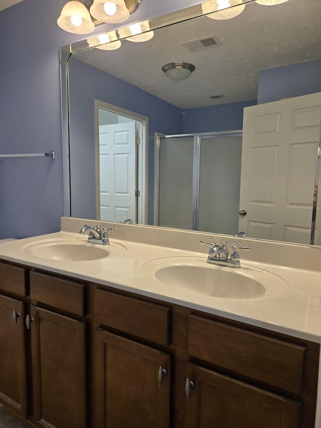 bathroom featuring double vanity, a stall shower, a sink, and visible vents