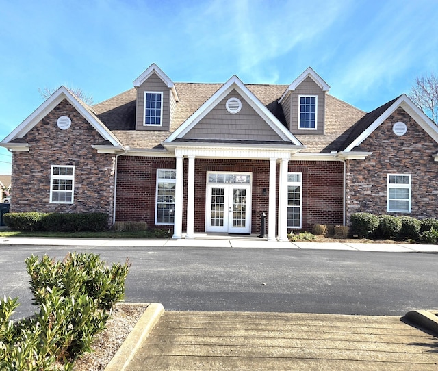 view of front facade featuring stone siding, french doors, brick siding, and a shingled roof