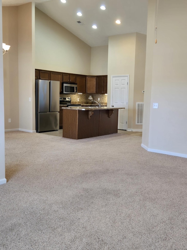 kitchen featuring a breakfast bar area, stainless steel appliances, visible vents, open floor plan, and a center island with sink