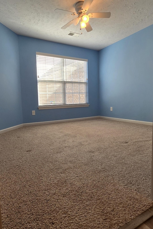 carpeted spare room featuring baseboards, a textured ceiling, visible vents, and a ceiling fan